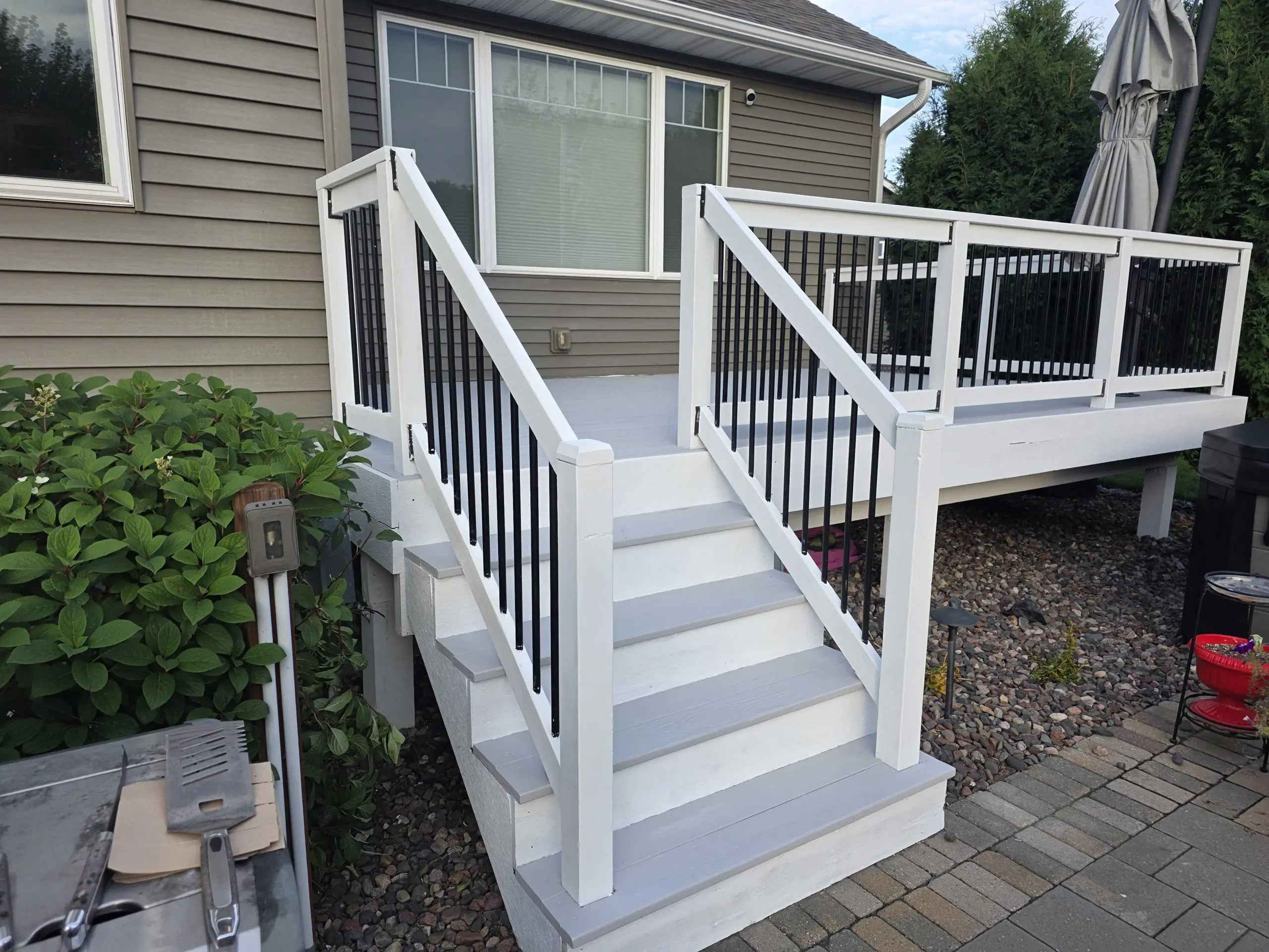 A newly painted white deck and stairs with black vertical railings contrasting against a gray-sided home, expertly finished by Local Painters in The Hills, TX