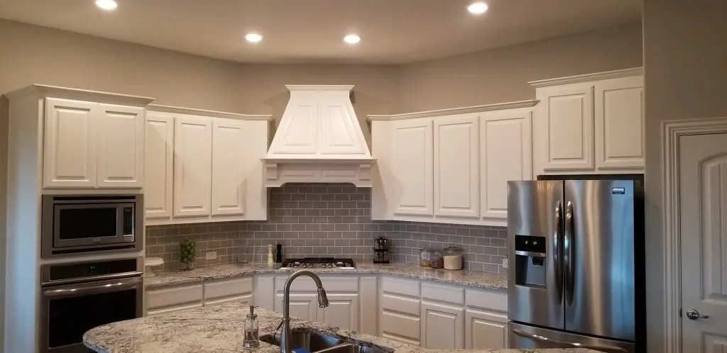 A bright, finished kitchen featuring white cabinets, a black island, stainless steel appliances, and a gray subway tile backsplash, remodeled by Texas Star Painting of Austin.