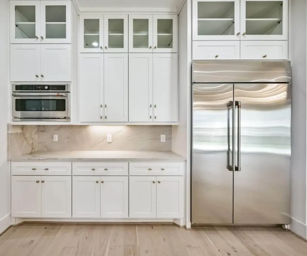 A clean, white pantry area featuring glass-front cabinets, a stainless steel refrigerator, and a marble slab backsplash, completed by Texas Star Painting of Austin.