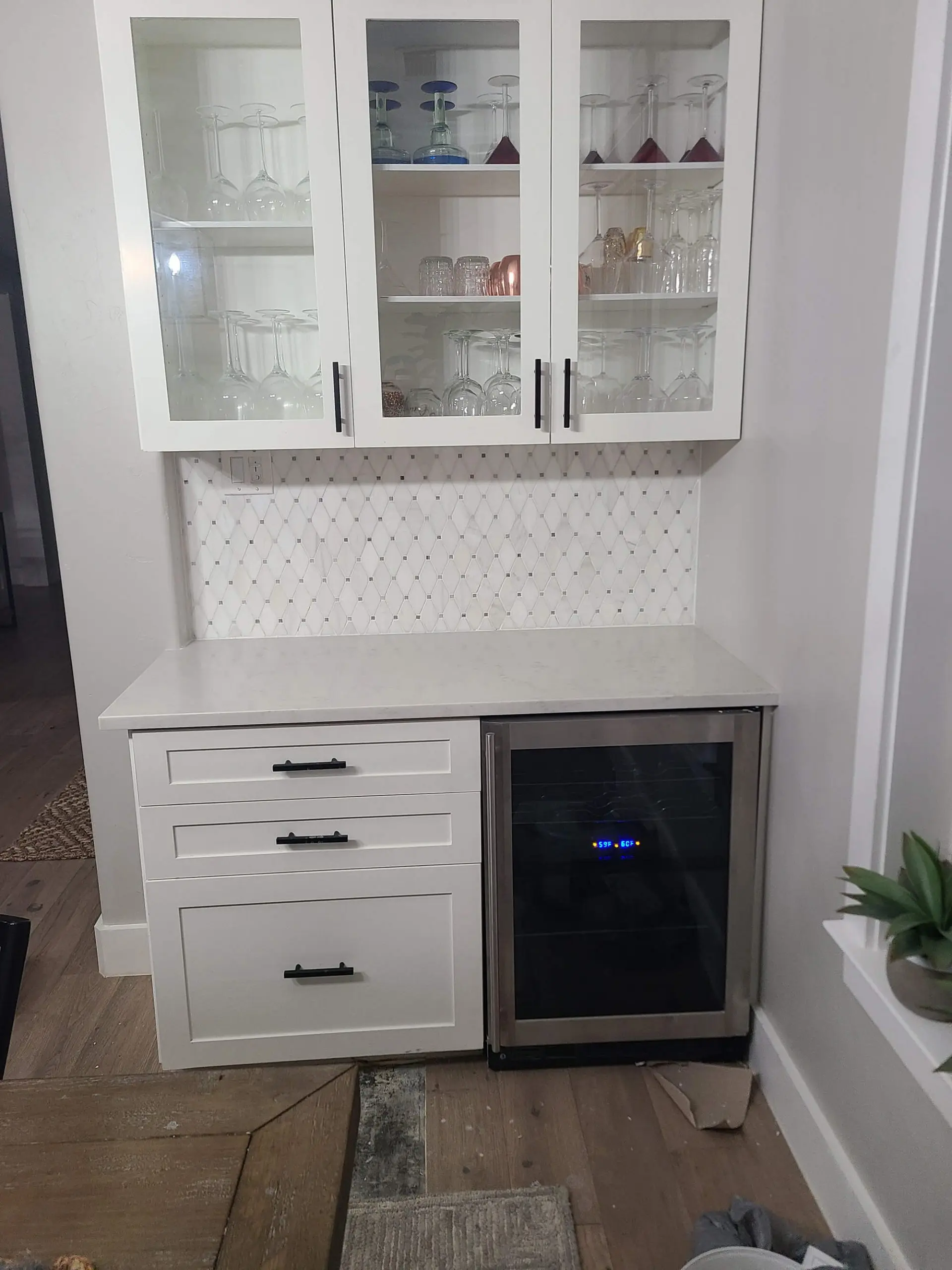 A crisp white custom wet bar with glass-front cabinets and wine fridge, featuring a diamond-patterned backsplash tile by Texas Star Painting of Austin.