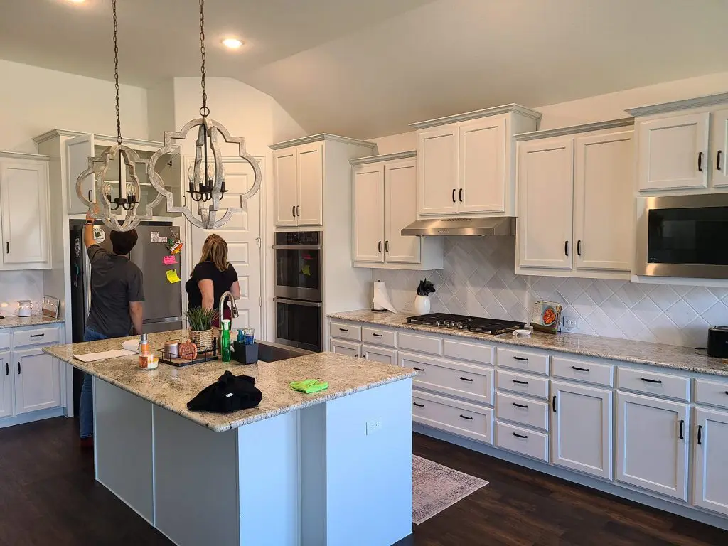 The final image shows a newly painted, bright white kitchen with Shaker-style cabinets, granite countertops, and two people working near the island, reflecting the clean, interior finishing standards of Texas Star Painting of Austin.