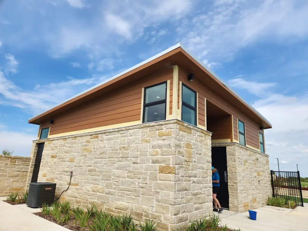 The modern utility building, featuring a stylish combination of brown horizontal siding and a stacked stone base, is ready for its expert finish by Texas Star Painting of Austin.