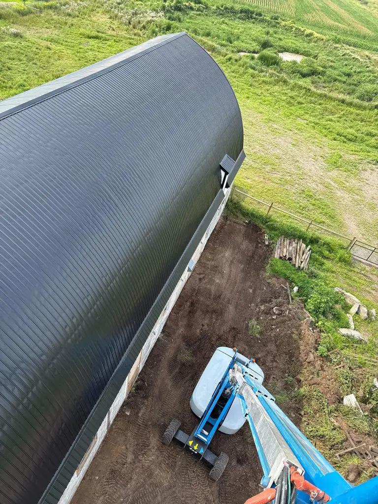 A freshly painted, deep charcoal Quonset hut roof stands out against the vibrant green fields, showcasing the high-reach quality work of Texas Star Painting of Austin.