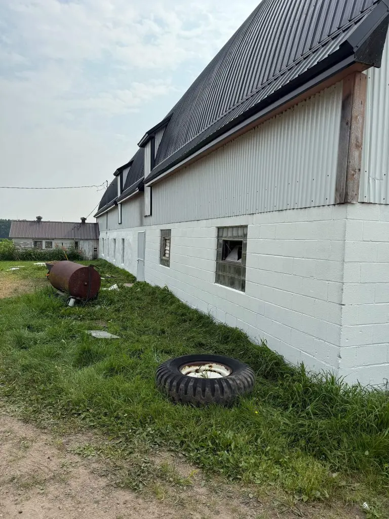 White barn with metal siding and some debris in the grass, captured by Texas Star Painting of Austin.