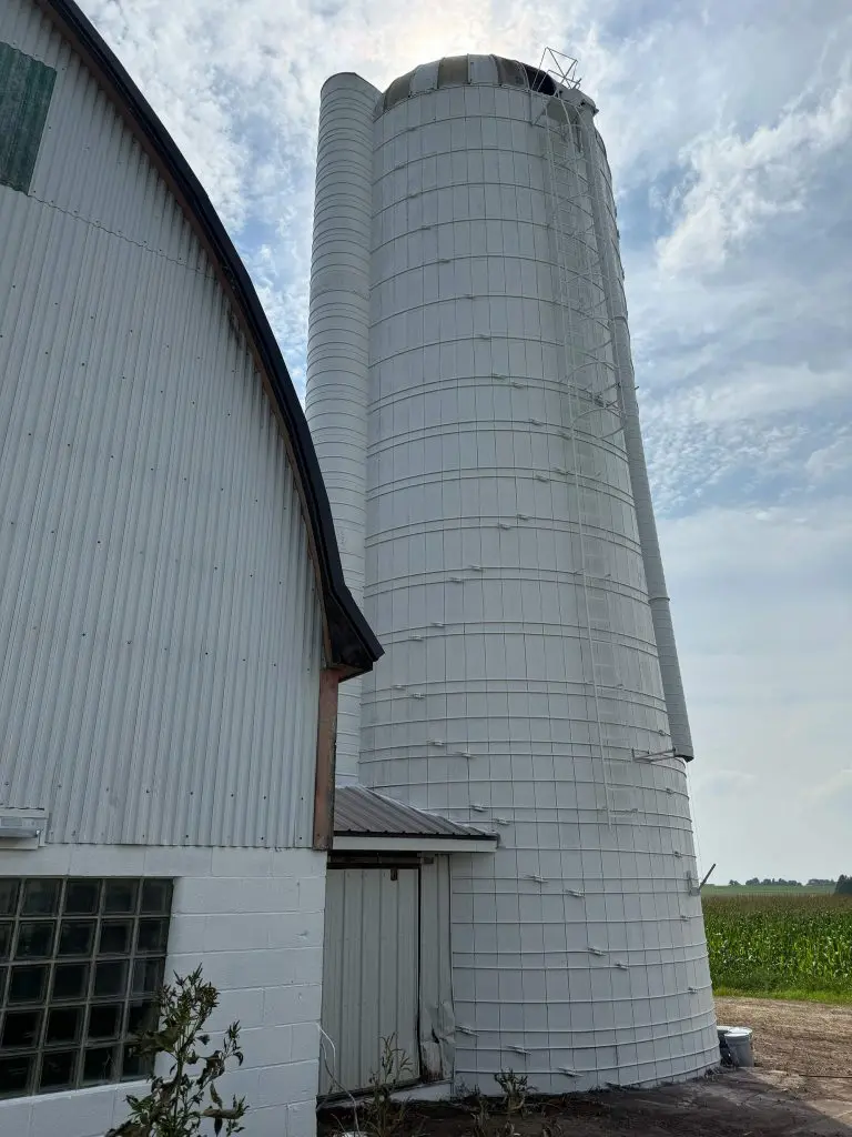 Weathered white farm silo and barn exterior standing against a bright sky and open fields, captured by Texas Star Painting of Austin.