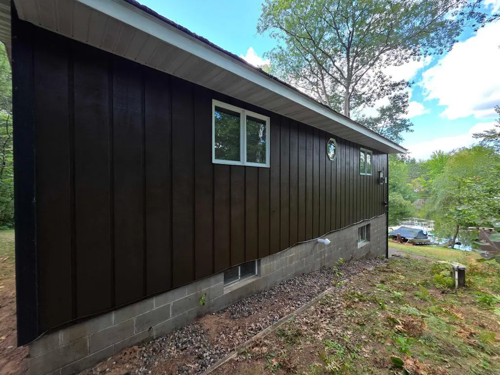A beautifully maintained, dark wood-sided lake house exterior with eye-catching red trim by Texas Star Painting of Austin.