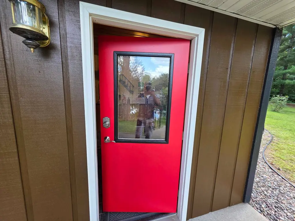 A bold, bright red entry door with a glass pane contrasting against brown siding, expertly painted by Texas Star Painting of Austin.