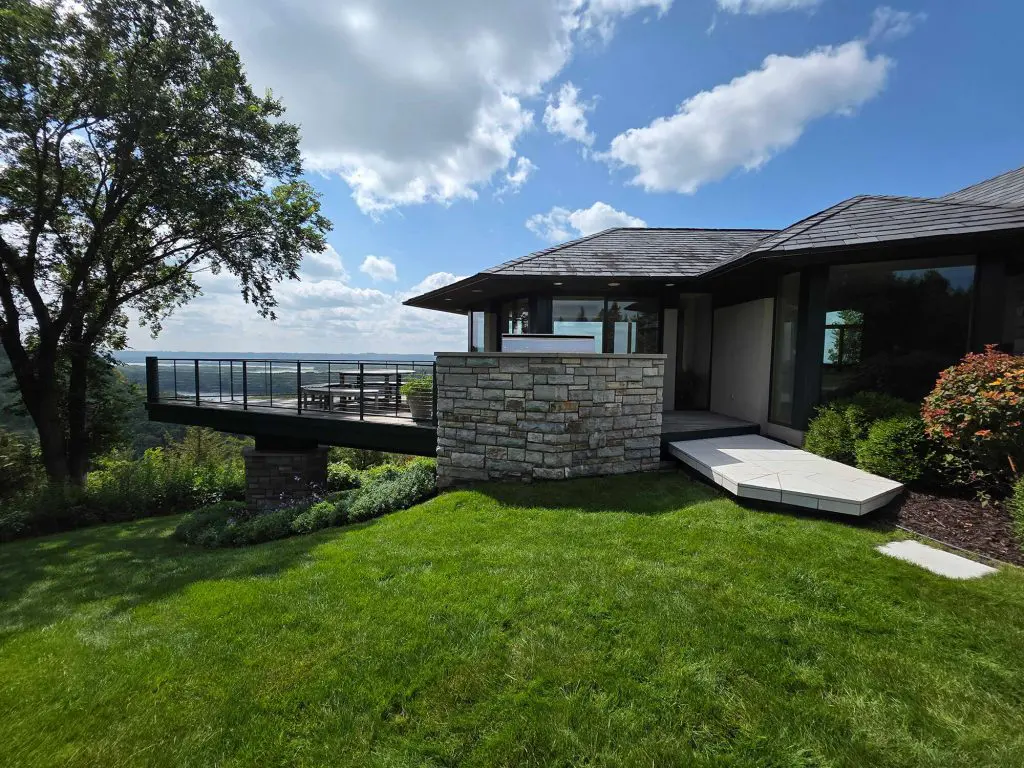 A stunning contemporary home with a stone facade, lush green lawn, and a cantilevered deck overlooking a panoramic view, showcasing the quality expected from Texas Star Painting of Austin.