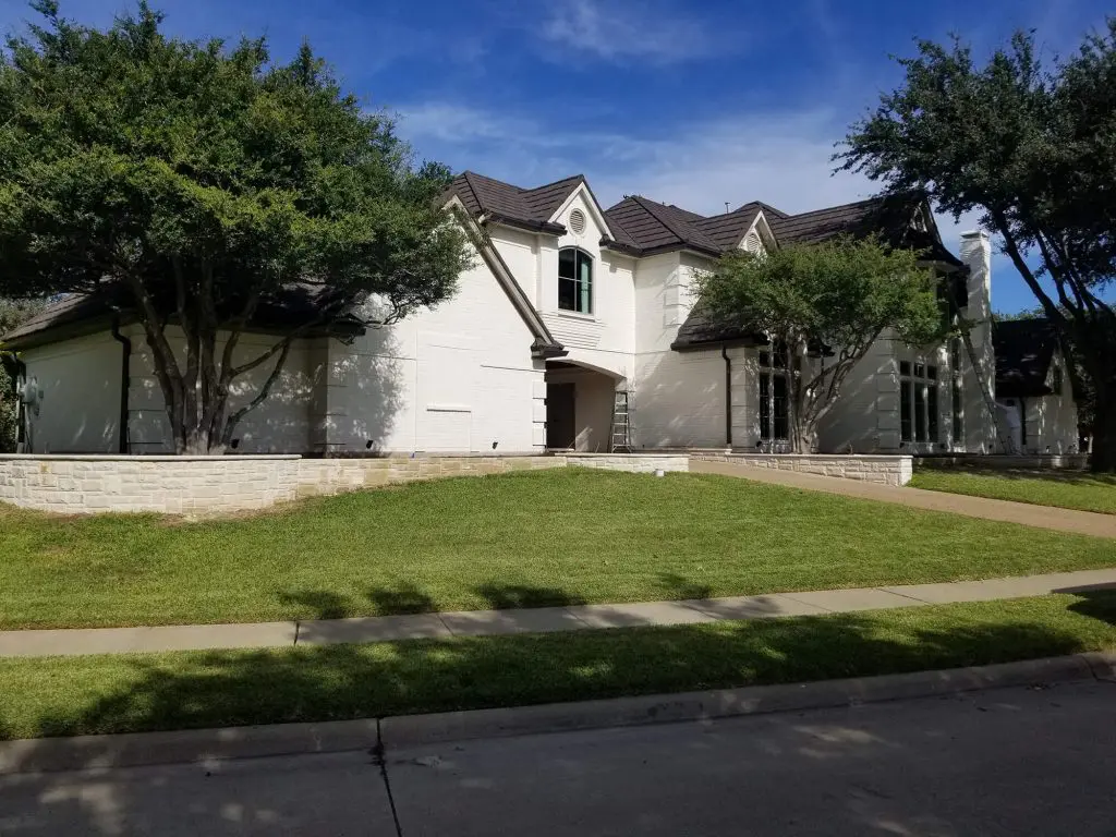 A majestic white home with a contrasting dark roof framed by lush green trees and lawn, expertly finished by Texas Star Painting of Austin.