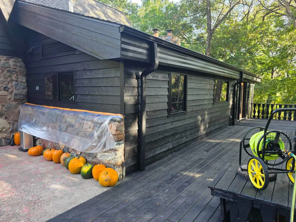 Black stained wood siding and deck on a forest house with stone accents and pumpkins.