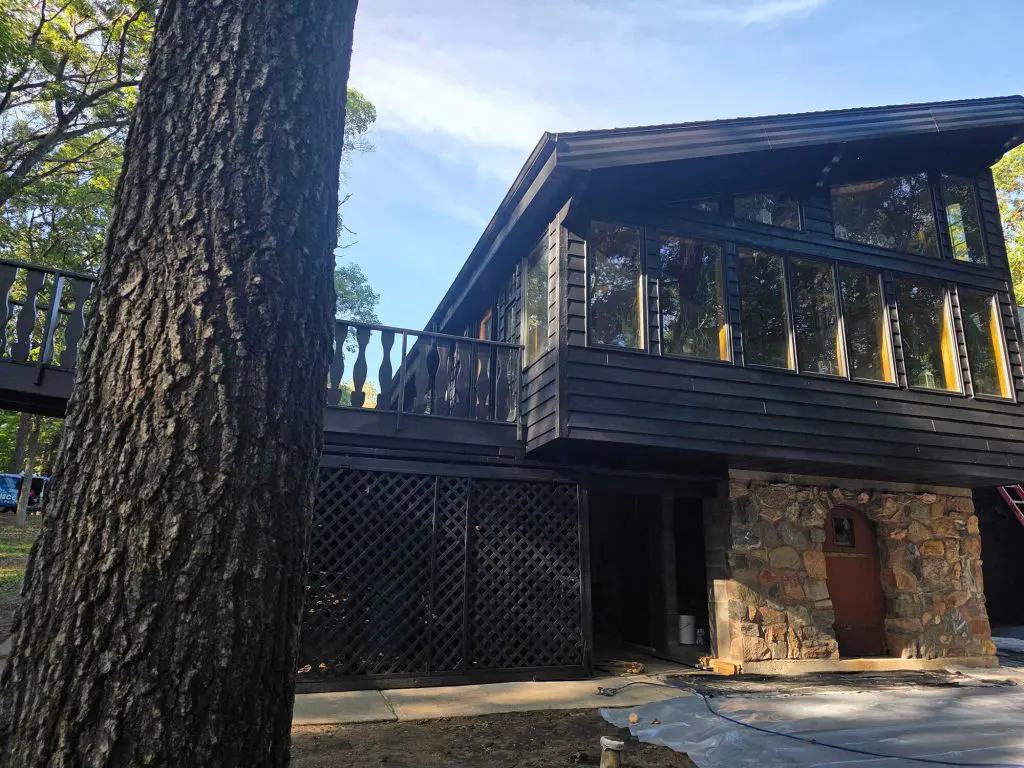 Black modern forest house with stone base and large windows.
