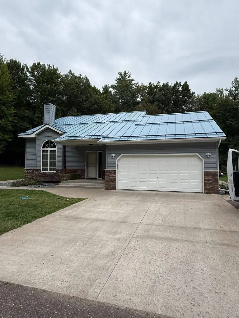 A modern single-story home with light gray siding, dark brick accents, and a distinctive bright blue metal roof, masterfully finished by Texas Star Painting of Austin.