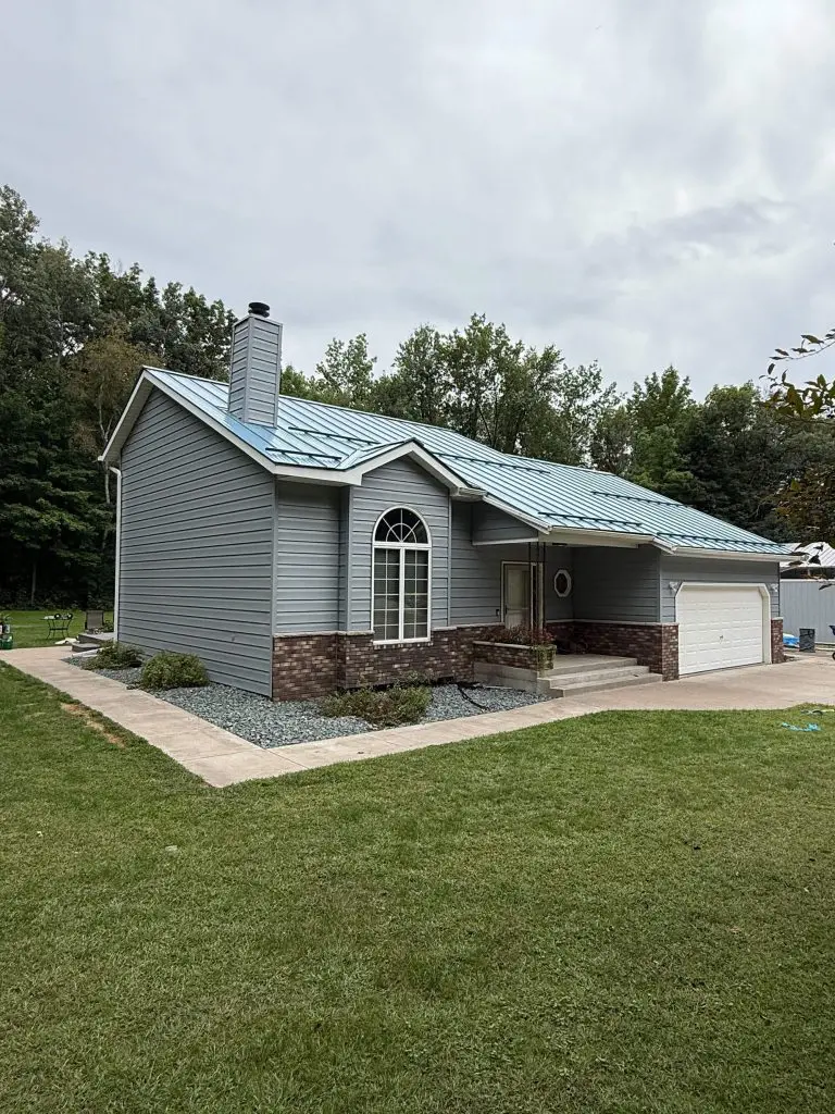 A contemporary home in gray siding with a striking blue metal roof and stone accents, beautifully enhanced by Texas Star Painting of Austin.