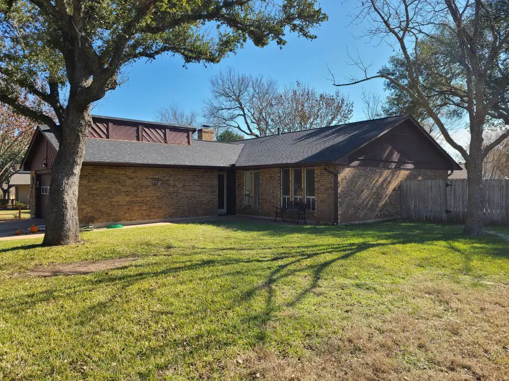 A welcoming ranch-style brick home nestled among large trees, showcasing quality paint work by Texas Star Painting of Austin.