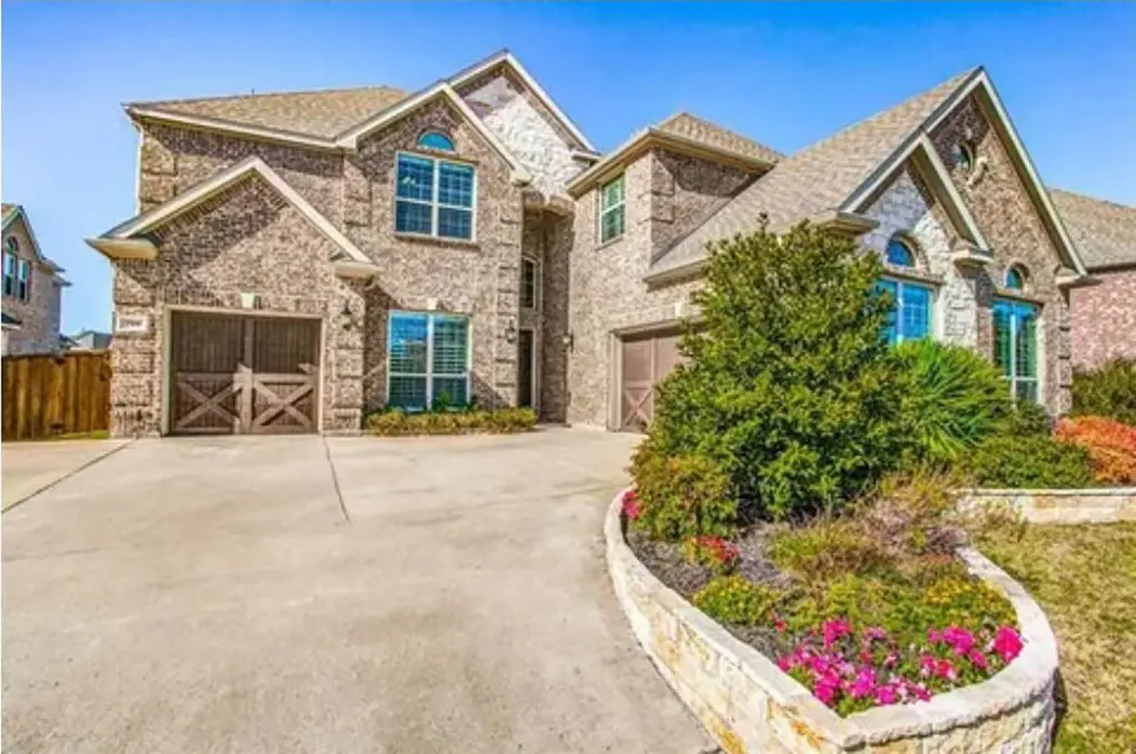 Large two-story brick house with light stone accents, multiple gables, arched windows, two separate garages with wooden doors