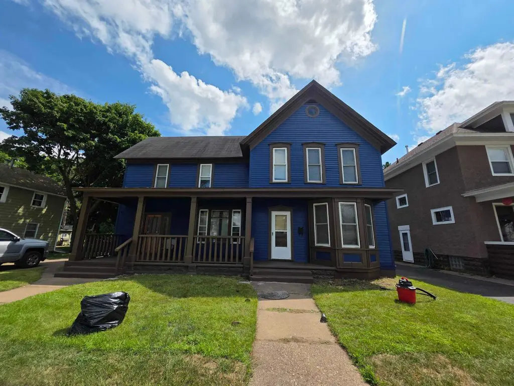 The deep blue siding and rich brown trim of this classic house glow under a bright summer sky, professionally finished by Texas Star Painting of Austin.