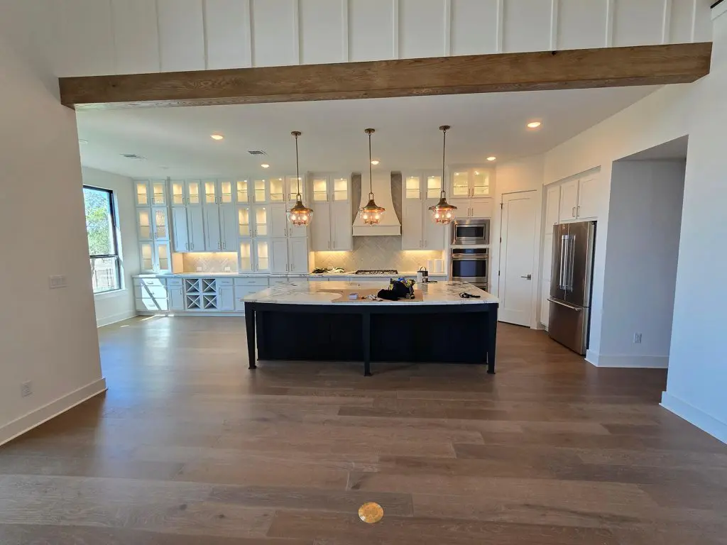 Modern open-concept kitchen with white cabinetry, a dark island, warm pendant lighting, and wood flooring, captured for Texas Star Painting of Austin.