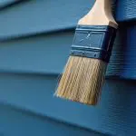 how to choose exterior paint finishes for your home with a brush applying blue paint to exterior siding