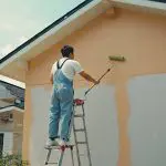 Painter applying fresh exterior paint to a home, showing how often should you repaint the exterior of your home based on surface condition and wear