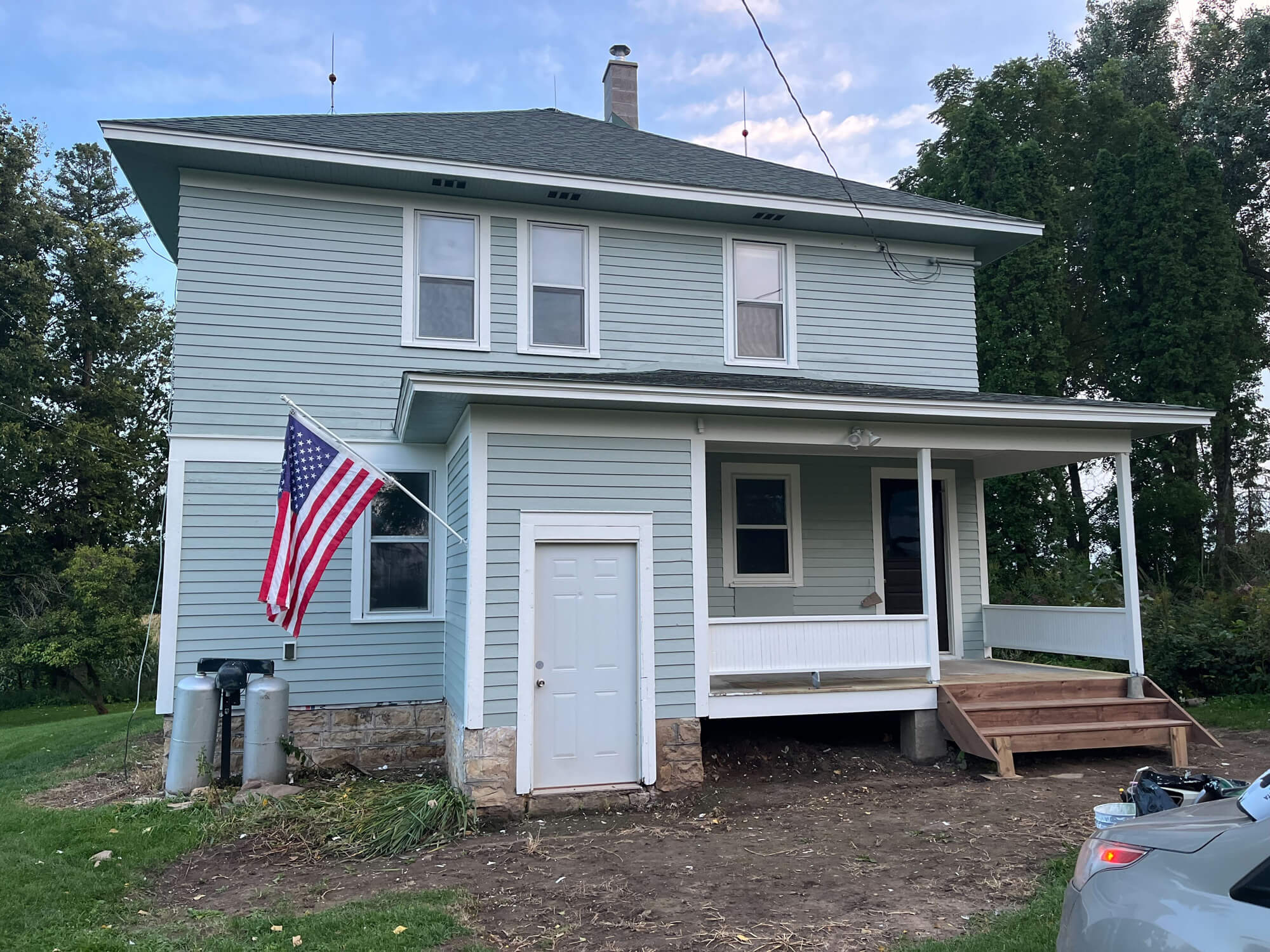 A historic, two-story farmhouse with an American flag proudly displayed features a fresh light blue exterior paint job from Texas Star Painting of Austin.