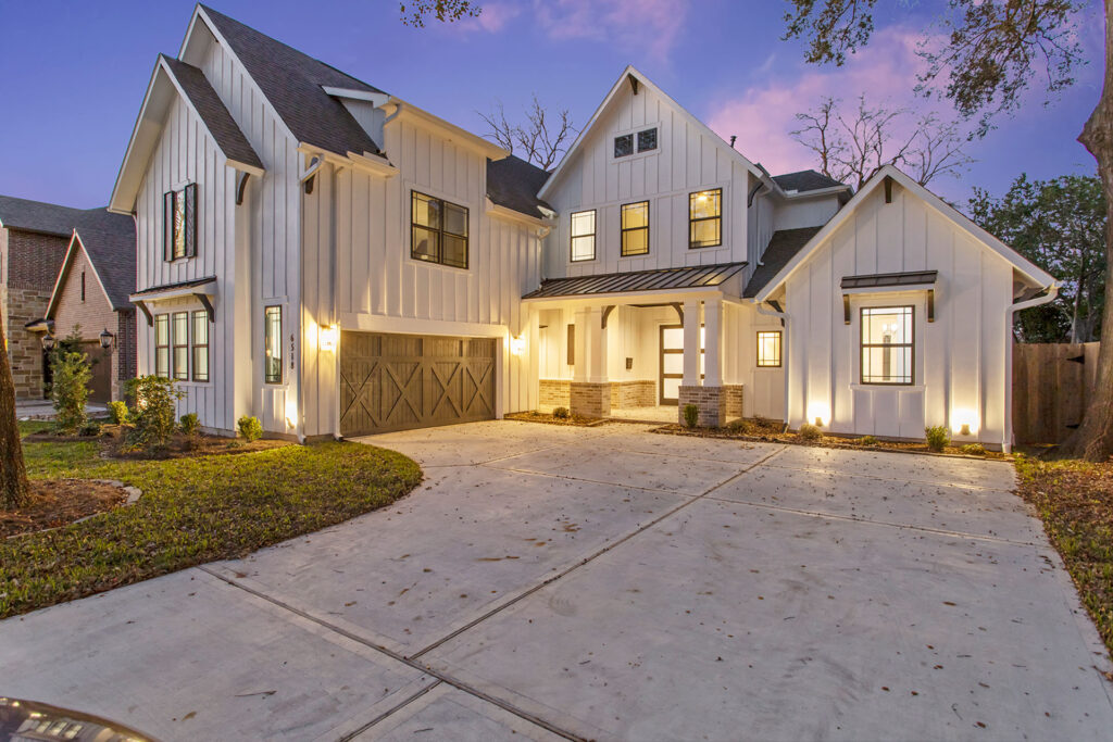 A grand, modern farmhouse exterior glows under twilight, illuminated to proudly display the exceptional painting expertise of Texas Star Painting of Austin.