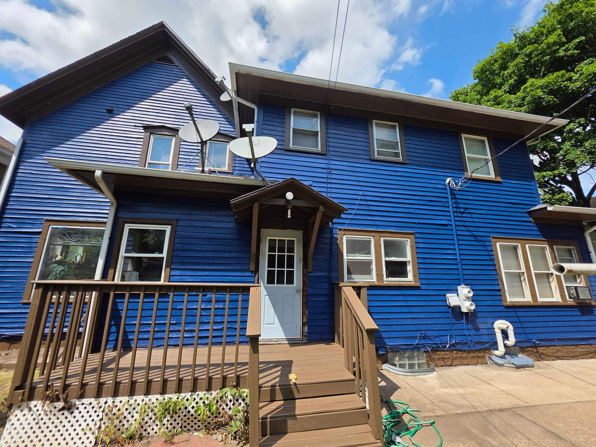 A striking blue multi-story home with contrasting brown trim and a matching wood deck, showcasing a bold exterior repaint by Texas Star Painting of Austin.