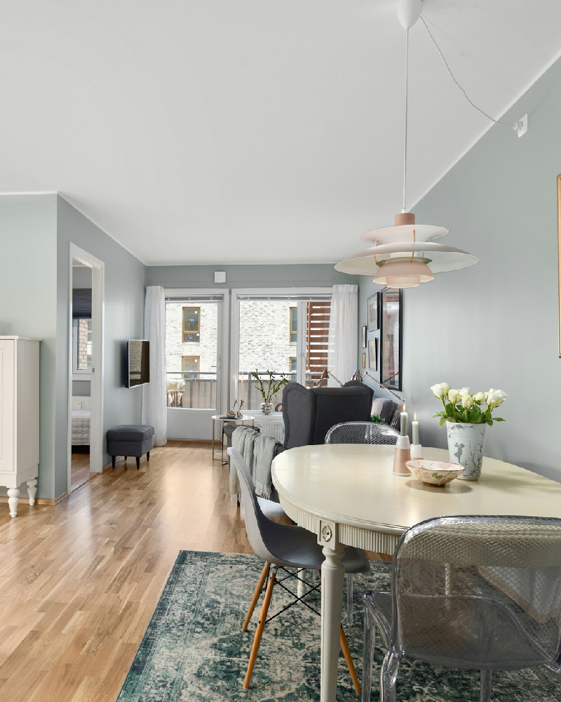 Bright interior repaint by Texas Star Painting of Austin featuring light blue walls, wood flooring, a decorative chandelier, and a white oval dining table in a modern apartment.
