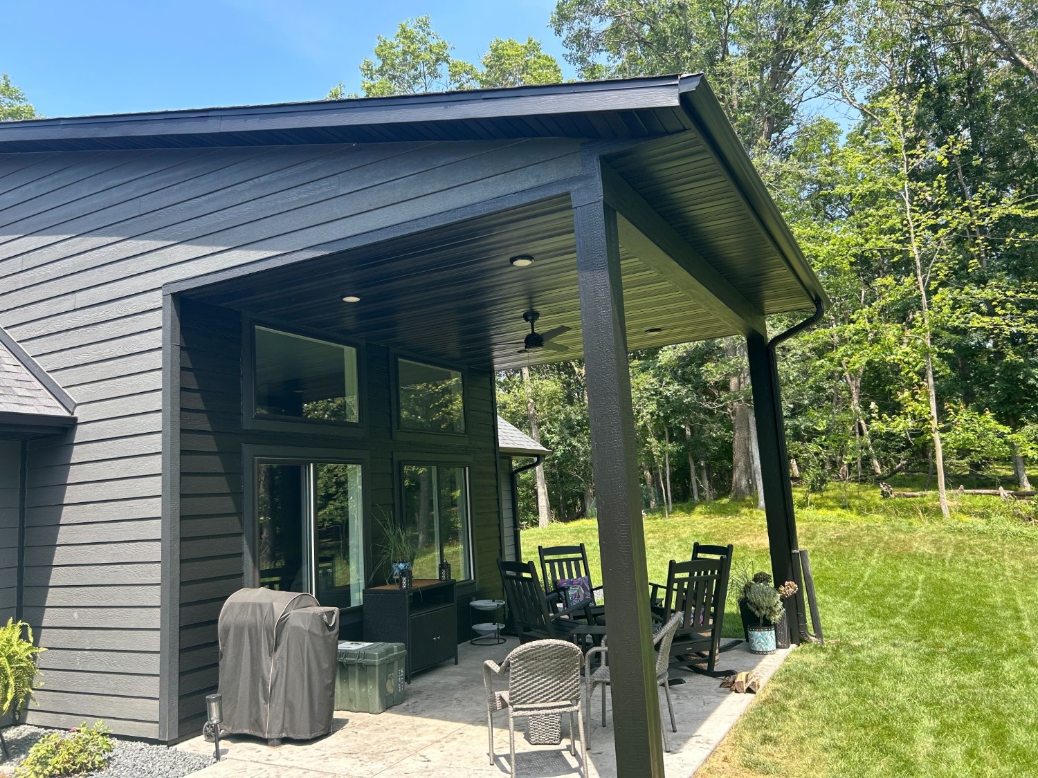A modern gray-painted home with a covered patio, outdoor seating, and a wooded backyard, freshly finished by painters in Driftwood, TX.
