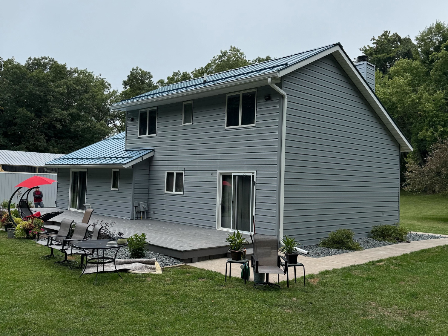A contemporary two-story house with cool gray siding and a light blue metal roof, featuring an expansive deck Local Painters in Wimberley, TX