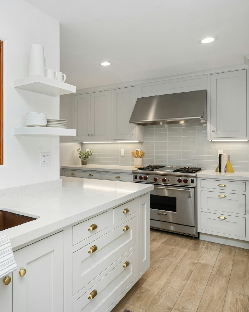 A bright modern kitchen with light gray cabinets, gold hardware, and a stainless steel range, showcasing the premium cabinet painting services