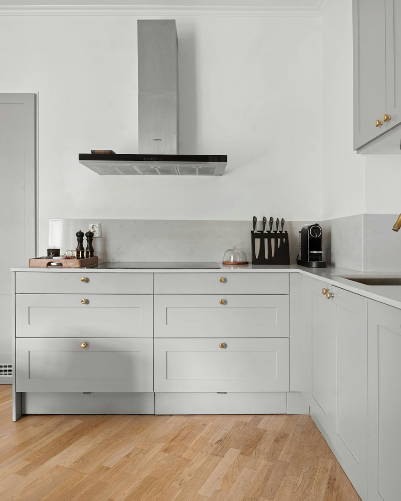 A spacious, open-concept living area and kitchen featuring a large gray sectional, white kitchen cabinets, and a gray island, demonstrating the quality interior and cabinet painting services of Texas Star Painting of Austin.