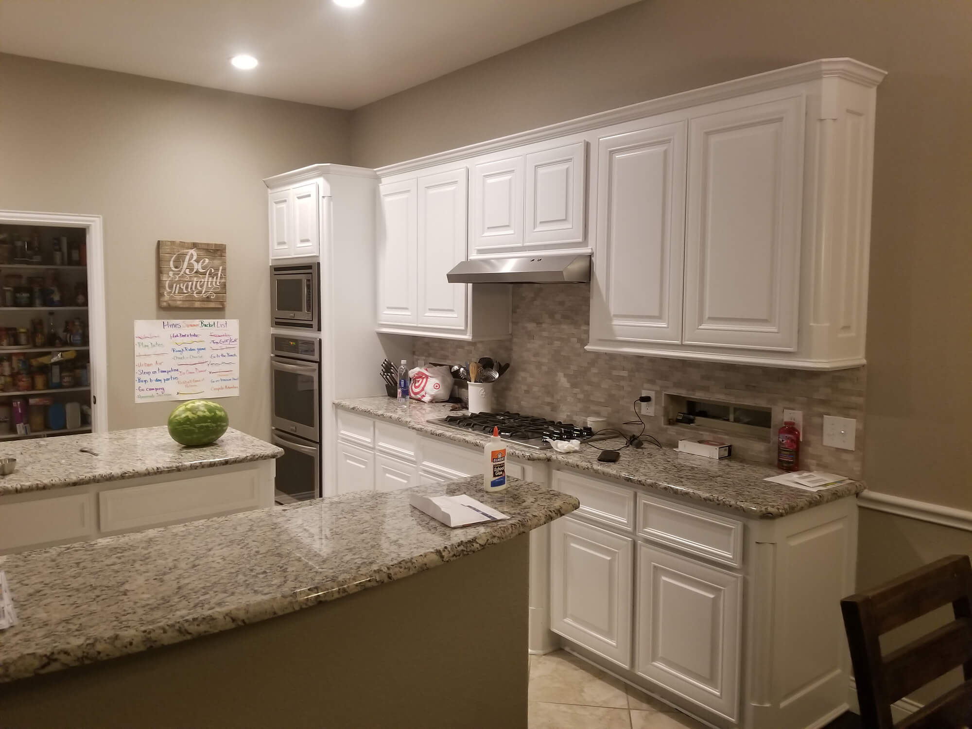 A freshly painted white kitchen with granite countertops, a tiled backsplash, and stainless steel double ovens, completed by Texas Star Painting of Austin.