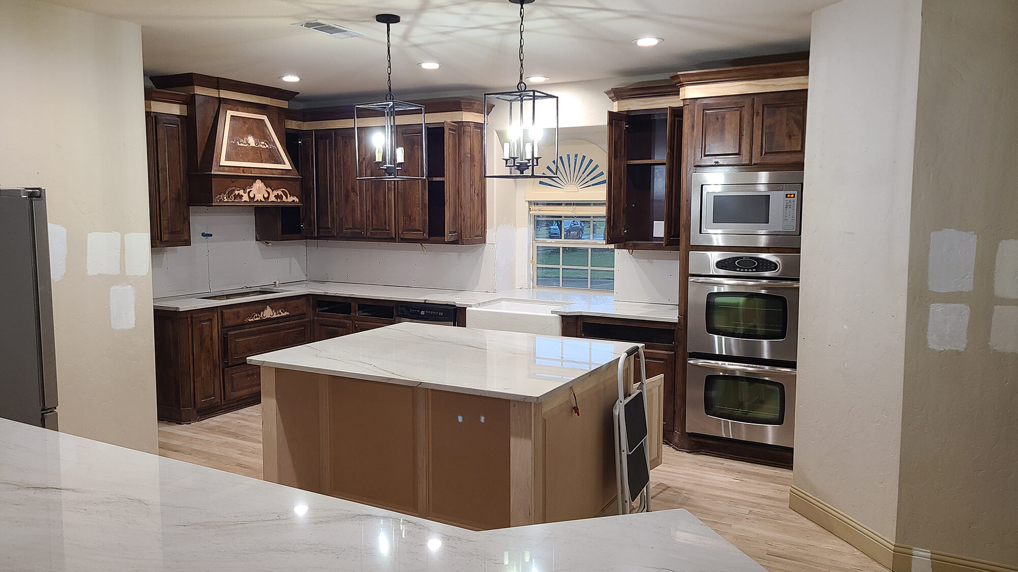A partially completed kitchen remodel featuring dark wood custom cabinets, a white marble island, and stainless steel appliances by Texas Star Painting of Austin.