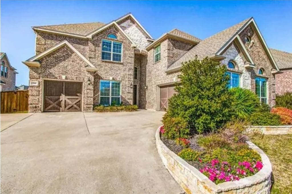 Large two-story brick house with light stone accents, multiple gables, arched windows, two separate garages with wooden doors