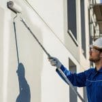 Commercial painter applying fresh exterior paint to a building wall illustrating when should a commercial building be repainted