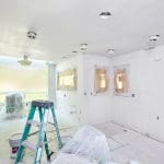 A room mid-renovation with a ladder, paint bucket, and covered surfaces showing the contrast between interior painting vs full renovation in progress.