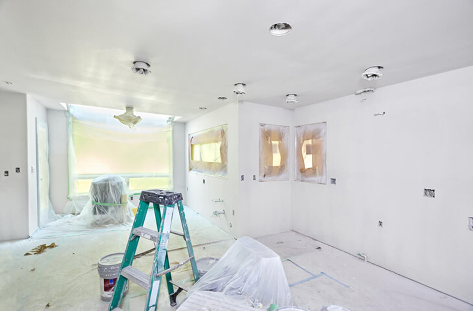 A room mid-renovation with a ladder, paint bucket, and covered surfaces showing the contrast between interior painting vs full renovation in progress.