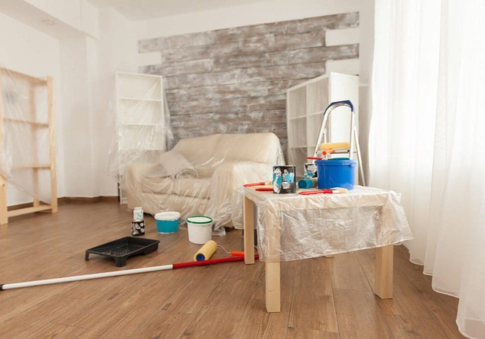 A protected living room with a distressed wood accent wall and painting supplies laid out, ready for a fresh new look by Texas Star Painting of Austin.
