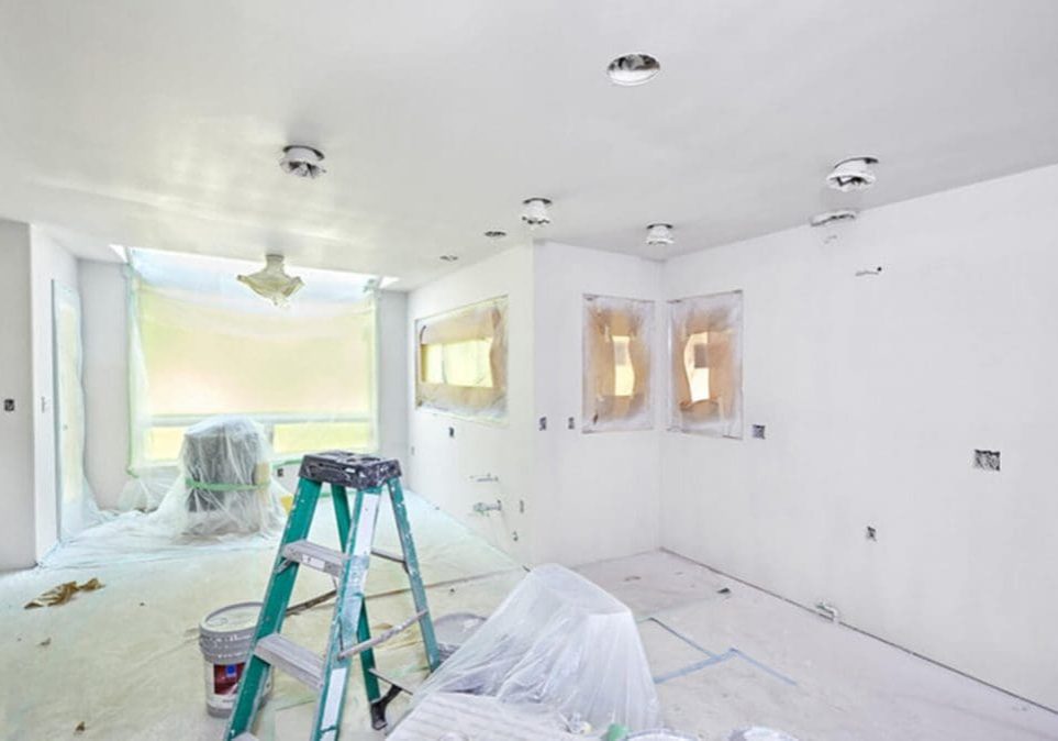 A room mid-renovation with a ladder, paint bucket, and covered surfaces showing the contrast between interior painting vs full renovation in progress.