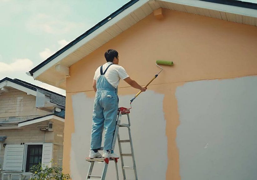 Painter applying fresh exterior paint to a home, showing how often should you repaint the exterior of your home based on surface condition and wear
